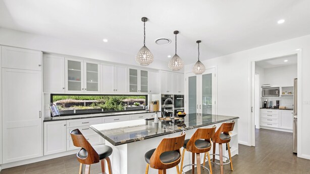 A modern kitchen with white cabinets, a large island with bar stools, and pendant lighting. - Casa Bella - Luxury 3 Bedroom Rural Retreat (Coffs Harbour)