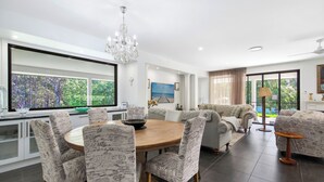 A modern living room with a dining area, large windows, and a chandelier. - Casa Bella - Luxury 3 Bedroom Rural Retreat (Coffs Harbour)