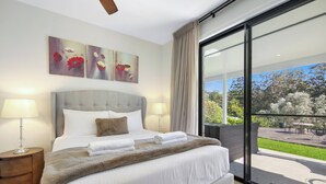 A bedroom with a large bed, two bedside lamps, a fluffy throw blanket, and a view of the outdoors through a sliding glass door. - Casa Bella - Luxury 3 Bedroom Rural Retreat (Coffs Harbour)