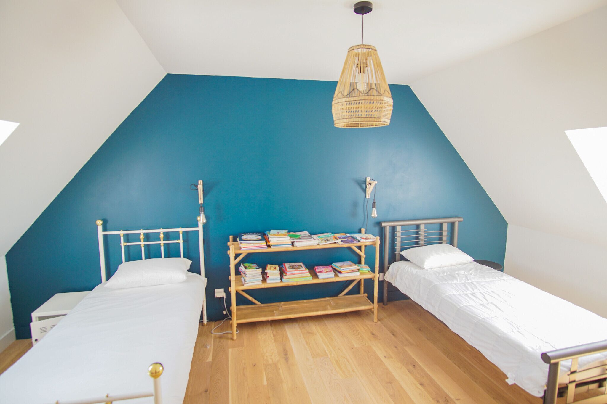 A room with two beds, a bookshelf, and a hanging light fixture.