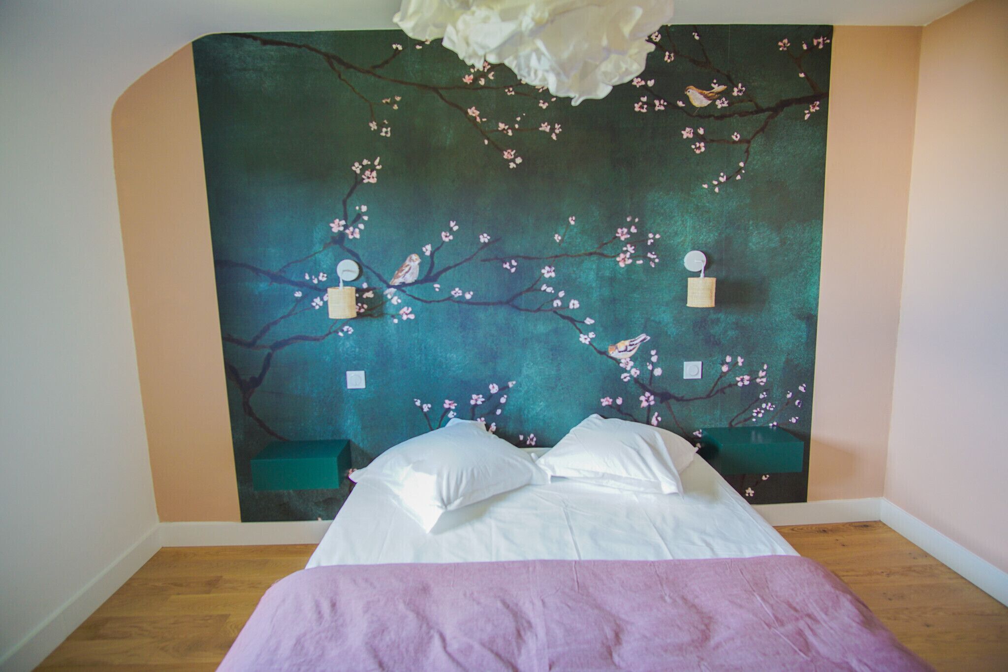 Une chambre à coucher avec un lit, une table de chevet et une fresque murale représentant des fleurs de cerisier.