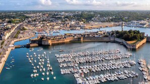 An aerial view of a harbor with numerous boats docked, a fortified structure, and a cityscape in the background. - -GAÏA- MAISON FAMILIALE VUE MER ET JARDIN DOURVEIL (Névez)