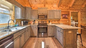 A kitchen with wooden cabinets, a stainless steel oven, granite countertops, and a window with blinds. - Private Cabin w/ Furnished Porch on < 3 Acres! (Mineral Bluff)
