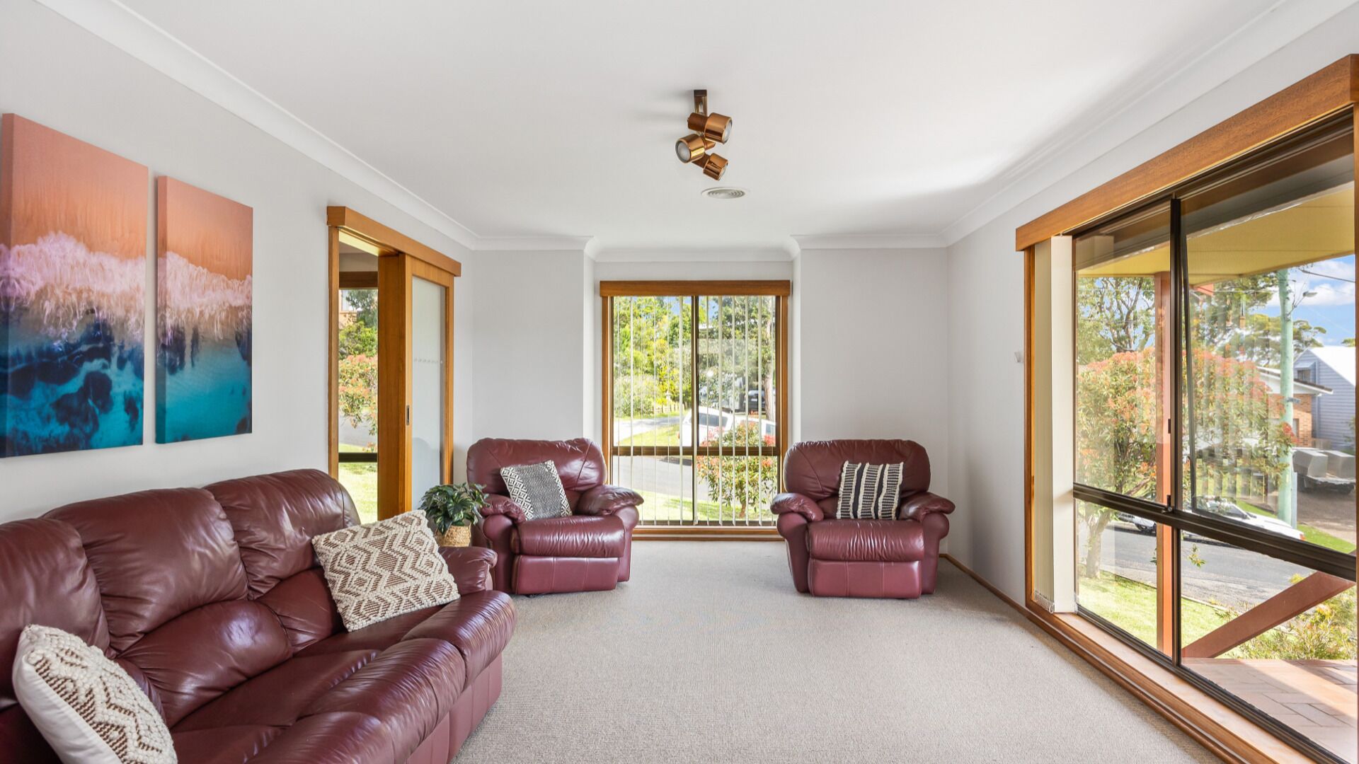 A spacious living room with a brown leather sofa, two armchairs, and a large window offering a view of the outdoors.