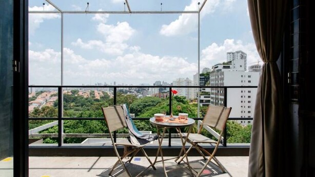 Ein Balkon mit Tisch und Stühlen, Blick auf eine Stadtlandschaft und einen klaren Himmel.