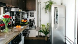 Eine Küche mit einem Edelstahl-Kühlschrank, einer gefliesten Rückwand und einer Arbeitsplatte mit Obstschale, Orangen und einer Blumenvase.