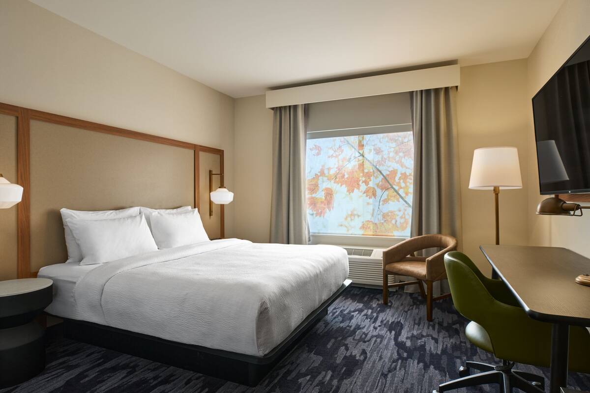 Een hotelkamer met een bed, een bureau, een stoel, een televisie en een raam met gordijnen.