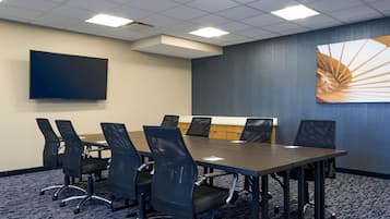 A conference room with a long table, six chairs, a flat-screen TV, and a large abstract painting on the wall.