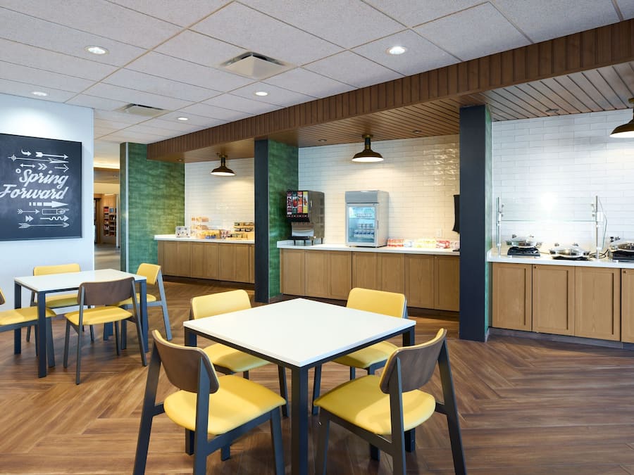 A modern restaurant with wooden flooring, yellow chairs, and a white table.