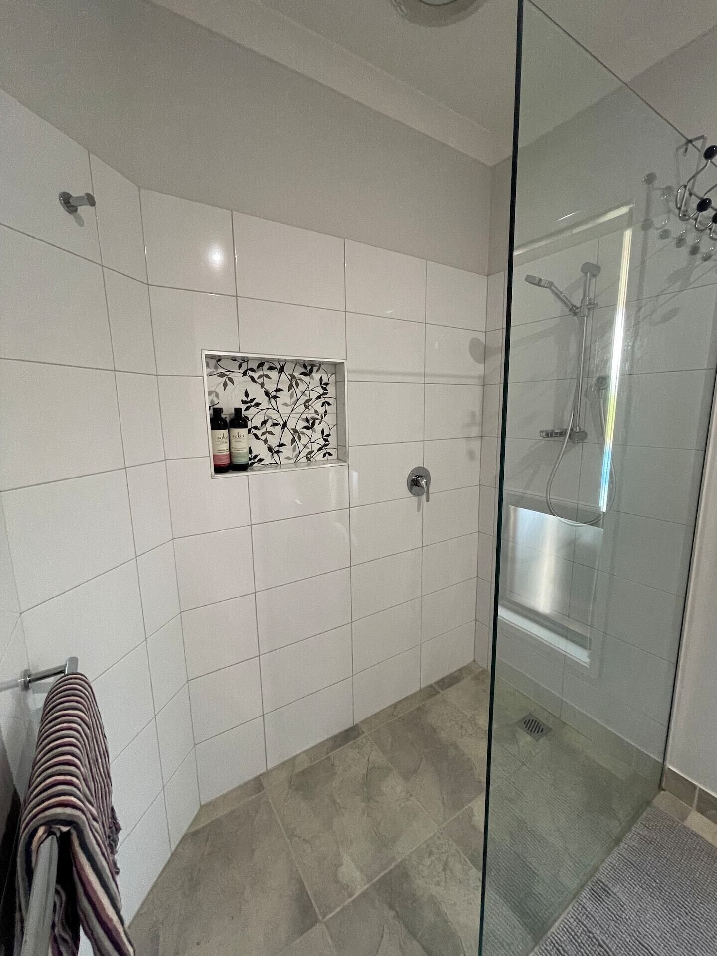 A modern bathroom with white tiles, a glass shower enclosure, and a towel rack.