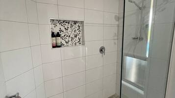 A modern bathroom with white tiles, a glass shower enclosure, and a towel rack.