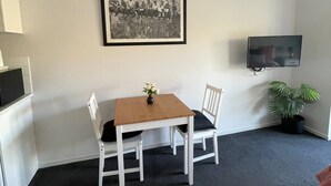 A room with a white table and chairs, a framed black and white photo on the wall, a TV mounted on the wall, and a potted plant. - River Gardens Axedale Pet friendly B & B Farm stay - Motel Room (Axedale)