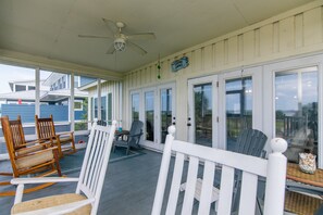 A covered porch with wooden rocking chairs, a table, and a ceiling fan. - Sound Choice:Oceanfront Home;Sunset Views/Dolphin Sightings on St. Helena Sound; Screened Porch (Edisto Beach)