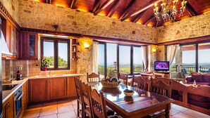 A rustic stone kitchen with wooden cabinets, a large dining table, and a television. - Traditional Holiday Villa with Panoramic View (Chania)
