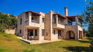 A two-story stone house with a balcony, a chimney, and a small patio area with outdoor furniture. - Traditional Holiday Villa with Panoramic View (Chania)