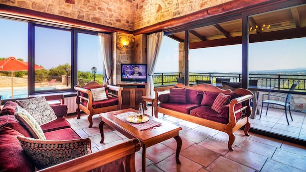 A spacious living area with a stone wall, large windows, and a pool view. - Traditional Holiday Villa with Panoramic View (Chania)