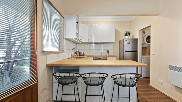 A modern kitchen with white cabinets, a wooden countertop, and three black bar stools. - Prosecco - Dinner Plain (Dinner Plain)