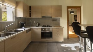 A modern kitchen with stainless steel appliances, wooden cabinets, and a bar area with black bar stools. - MisaraliotouA3 · 3BR Prime APT a breath away from (Athens)