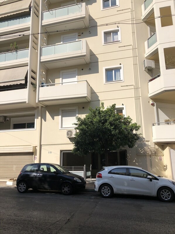 A multi-story residential building with balconies, a tree in front, and two cars parked in front. - MisaraliotouA3 · 3BR Prime APT a breath away from (Athens)