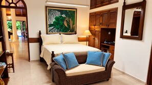 Ein Hotelzimmer mit einem Bett, einem Korbsessel mit Kissen, einem Bild an der Wand und einem Kleiderschrank mit Spiegel.