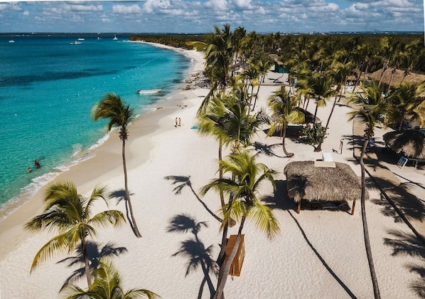 A beach with palm trees, a thatched lounge area, and a clear view of the ocean. - Villa Casa Nostra by KlabHouse 5BDRM w/Pool and Chef (La Romana)
