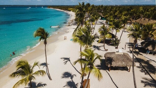 Ein Strand mit weißem Sand, Palmen und klarem türkisblauem Wasser.