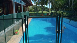 Ein Swimmingpool mit grünem Zaun, umgeben von einem Garten und einem Gebäude mit Holzfassade.