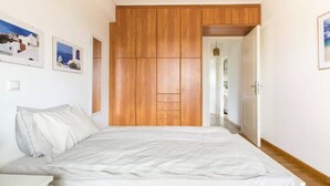 A bedroom with a bed, wooden wardrobe, and a door leading to another room. - Compact 3 room apartment in Mall Athens. (Marousi)