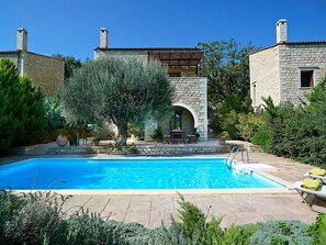 Relax by the serene pool surrounded by lush gardens and a traditional stone building.