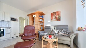 Una sala de estar moderna con un sillón de cuero, un sofá gris, una estantería de madera y una mesita con una planta.