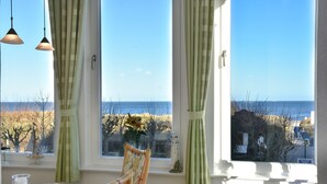 Una habitación con vista al mar, una mesa con un vaso, una silla y dos lámparas colgantes.