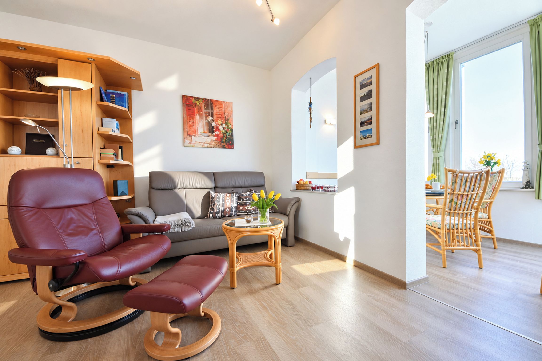 A modern living room with a leather chair, a grey sofa, a wooden side table, and a dining area with wicker chairs.