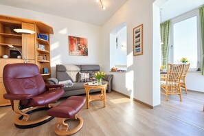 A modern living room with a leather chair, a grey sofa, a wooden side table, and a dining area with wicker chairs. - Meerblick 05 House - with a direct view of the sea (Ahlbeck (Seebad))