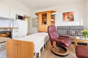 A compact living space with a kitchenette, a dining area, a seating area with a sofa and armchair, and a painting on the wall. - Meerblick 05 House - with a direct view of the sea (Ahlbeck (Seebad))