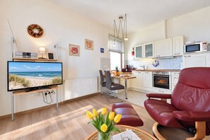 A modern living room with a flat-screen TV, a red leather chair, a dining area with a table and chairs, a kitchen with white cabinets and a microwave, and a fireplace. - Meerblick 05 House - with a direct view of the sea (Ahlbeck (Seebad))