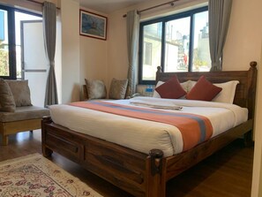A neatly made bed with a striped blanket, a wooden headboard, and a bedside table with a lamp. - Hotel Ramanam (Kathmandu)