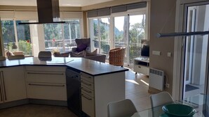 Une cuisine moderne avec une table à manger en verre, un four encastré et une grande fenêtre donnant sur un jardin.