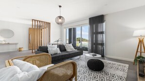 Een moderne woonkamer met een bank, twee rieten fauteuils, een bijzettafeltje en een vloerkleed met een patroon.
