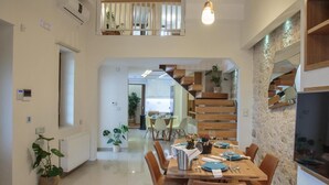 A modern dining area with a wooden staircase, a kitchen in the background, and potted plants. - Unique vacation in traditional Cretan village in the mountains with family (Zaros)