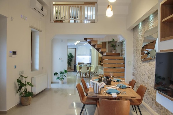 A modern dining area with a wooden staircase, a kitchen in the background, and potted plants.