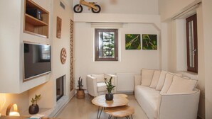 A living room with a flat-screen TV, a sofa, a coffee table, a fireplace, and a motorcycle decoration. - Unique vacation in traditional Cretan village in the mountains with family (Zaros)