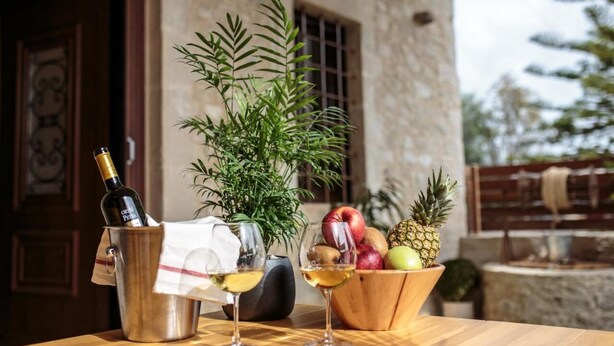A table with a bottle of wine, two glasses, a bowl of fruit, and a potted plant. - Unique vacation in traditional Cretan village in the mountains with family (Zaros)