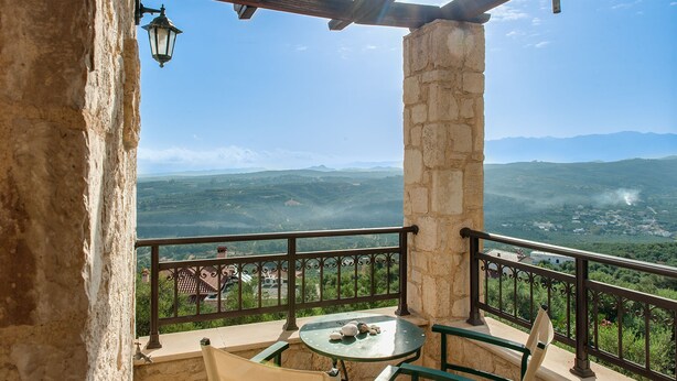Ein Balkon mit einer Steinsäule, einem Tisch aus Stein und Blick auf eine gebirgige Landschaft.
