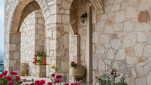 Ein Gebäude aus Stein mit Bögen und einer Laterne. Blumentöpfe mit Blumen und Blick auf das Meer.