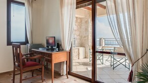 Ein Zimmer mit einem Holztisch, einem Computer und einem Stuhl. Es gibt ein Fenster und einen Blick auf einen Balkon mit Sitzgelegenheiten.
