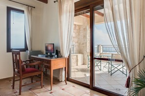 Une pièce avec un bureau en bois, un ordinateur et une chaise. Il y a une fenêtre et une vue sur un balcon extérieur avec des chaises.