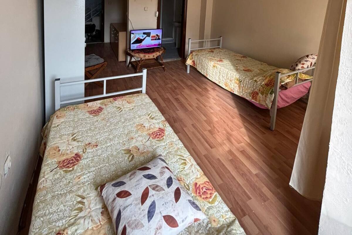 Quarto tipo dormitório com duas camas de solteiro, uma televisão sobre uma mesinha e um guarda-roupa.