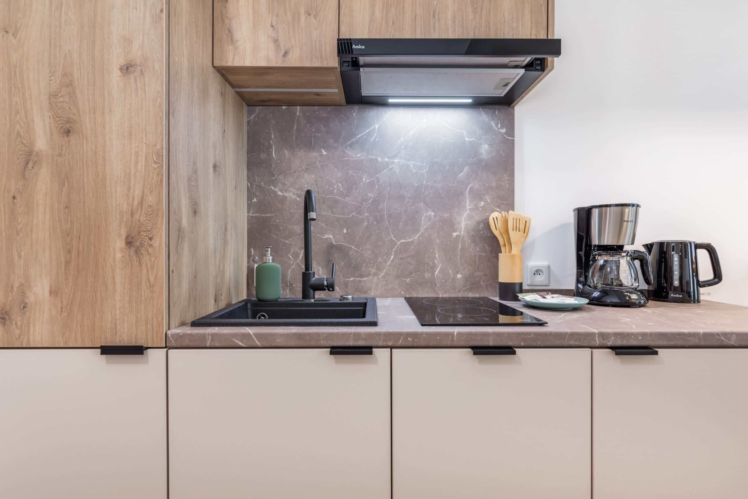 A modern kitchen with a black range hood, a sink, a stove, and a coffee maker.