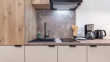 A modern kitchen with a black range hood, a sink, a stove, and a coffee maker.