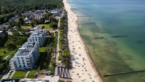 An aerial view of a coastal area with a beach, residential buildings, and a clear view of the ocean.